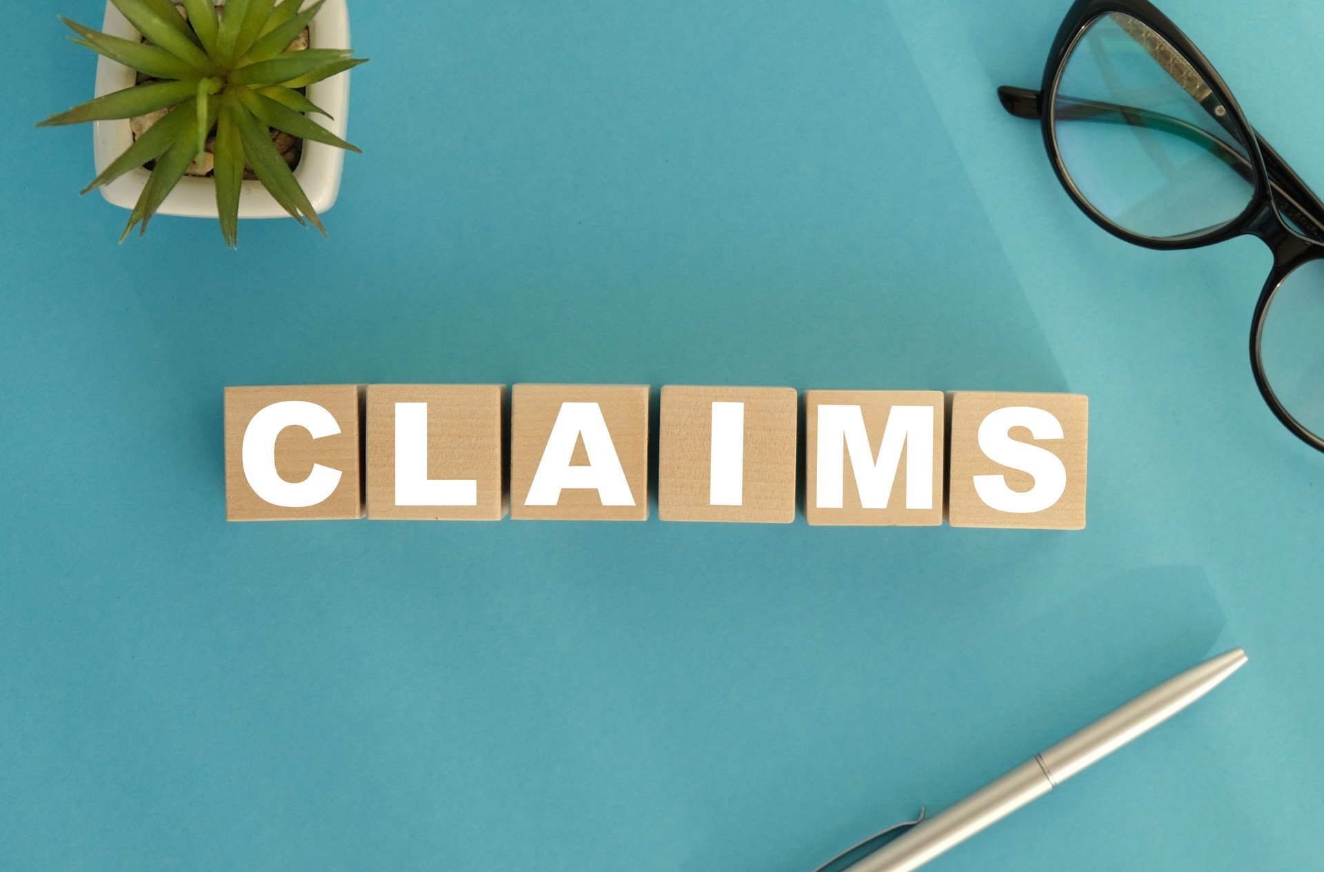 On a light background between the calculator and the pen there are wooden cubes with the word CLAIMS. Business concept.